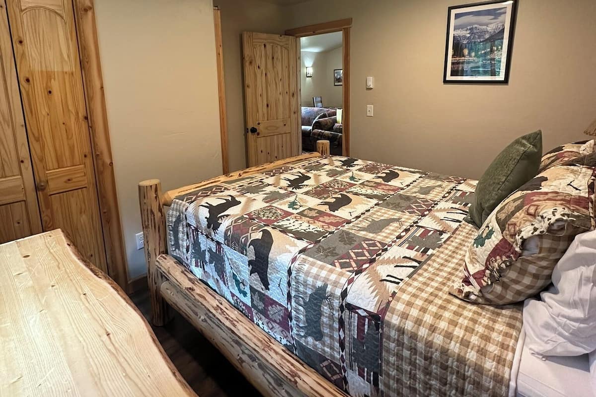 A bedroom with a wooden bed, a wooden table, and a door leading to another room.