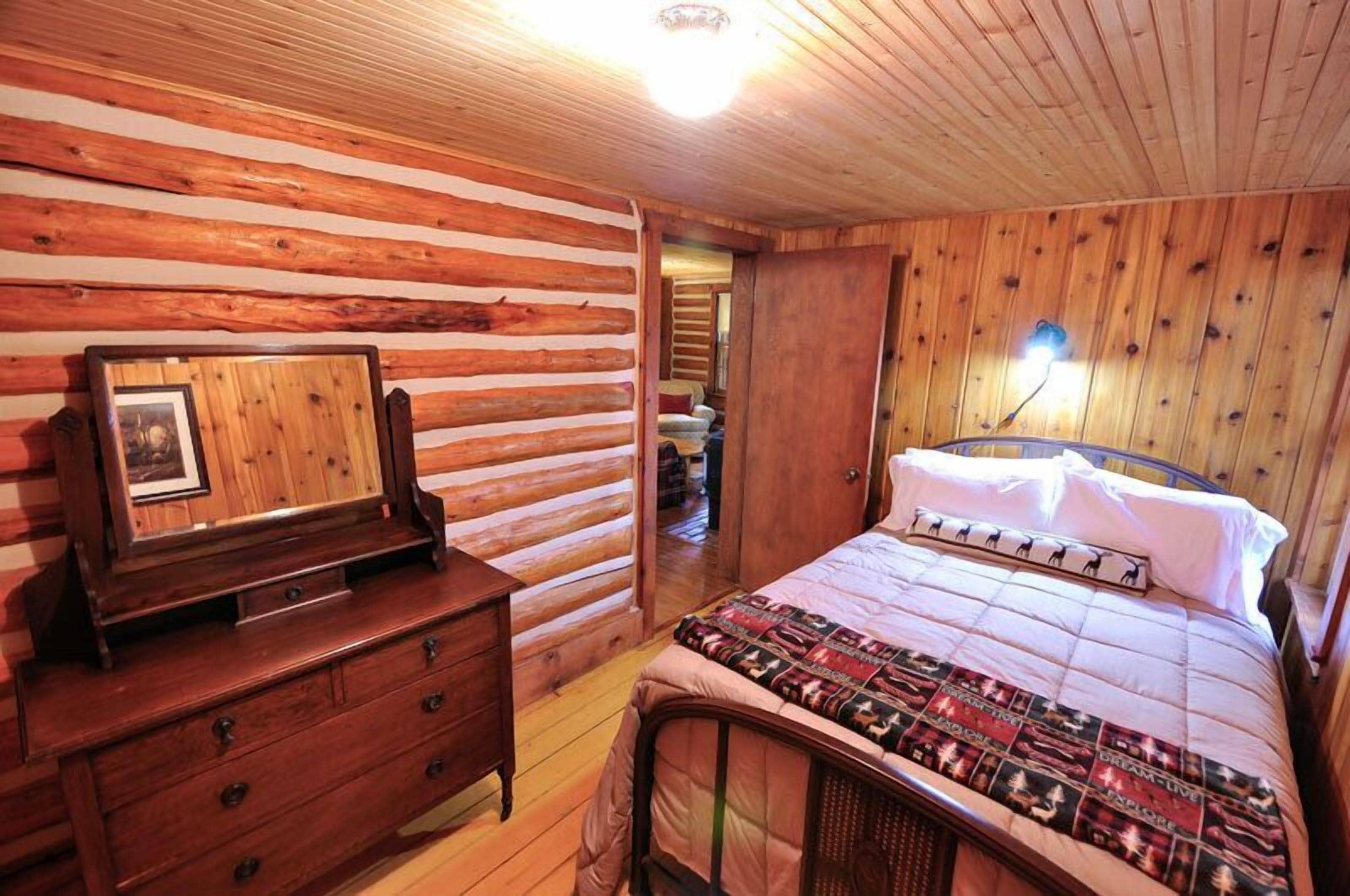 A wooden cabin-style bedroom with a bed, dresser, and a framed picture on the wall.