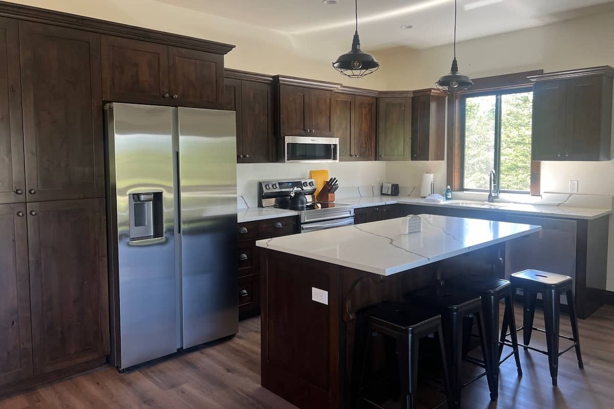 A modern kitchen with dark wooden cabinets, stainless steel appliances, and a central island with bar stools.