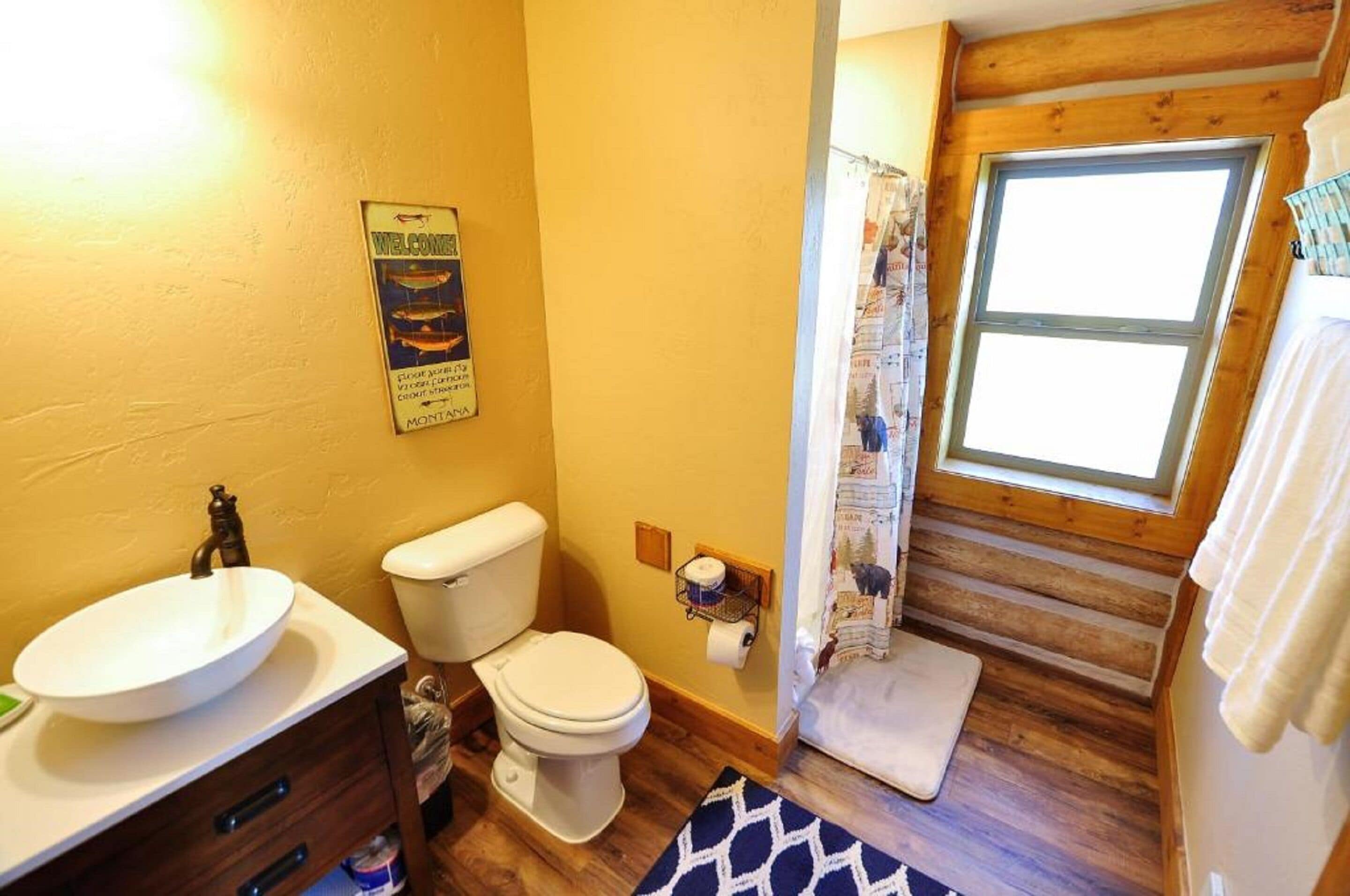 A compact bathroom with a wooden floor, a white sink, a toilet, and a shower curtain.