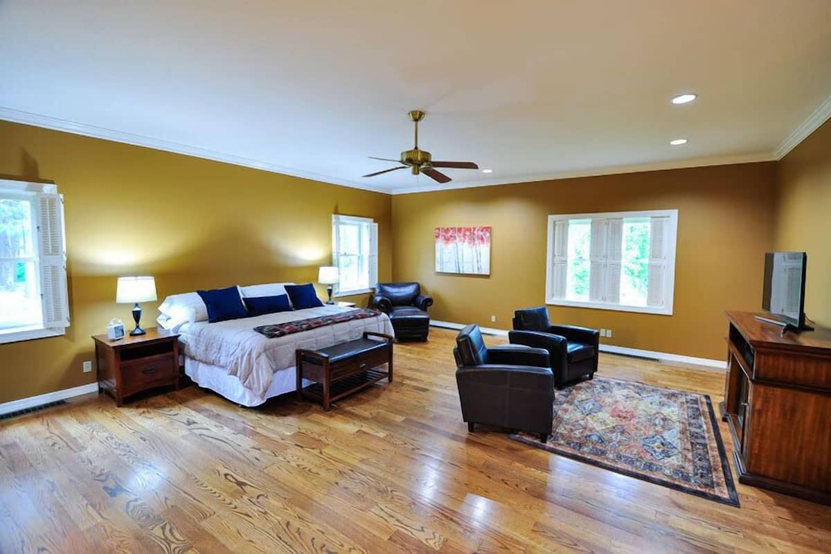 A bedroom with a bed, bedside tables, a desk, a chair, a ceiling fan, and a television.