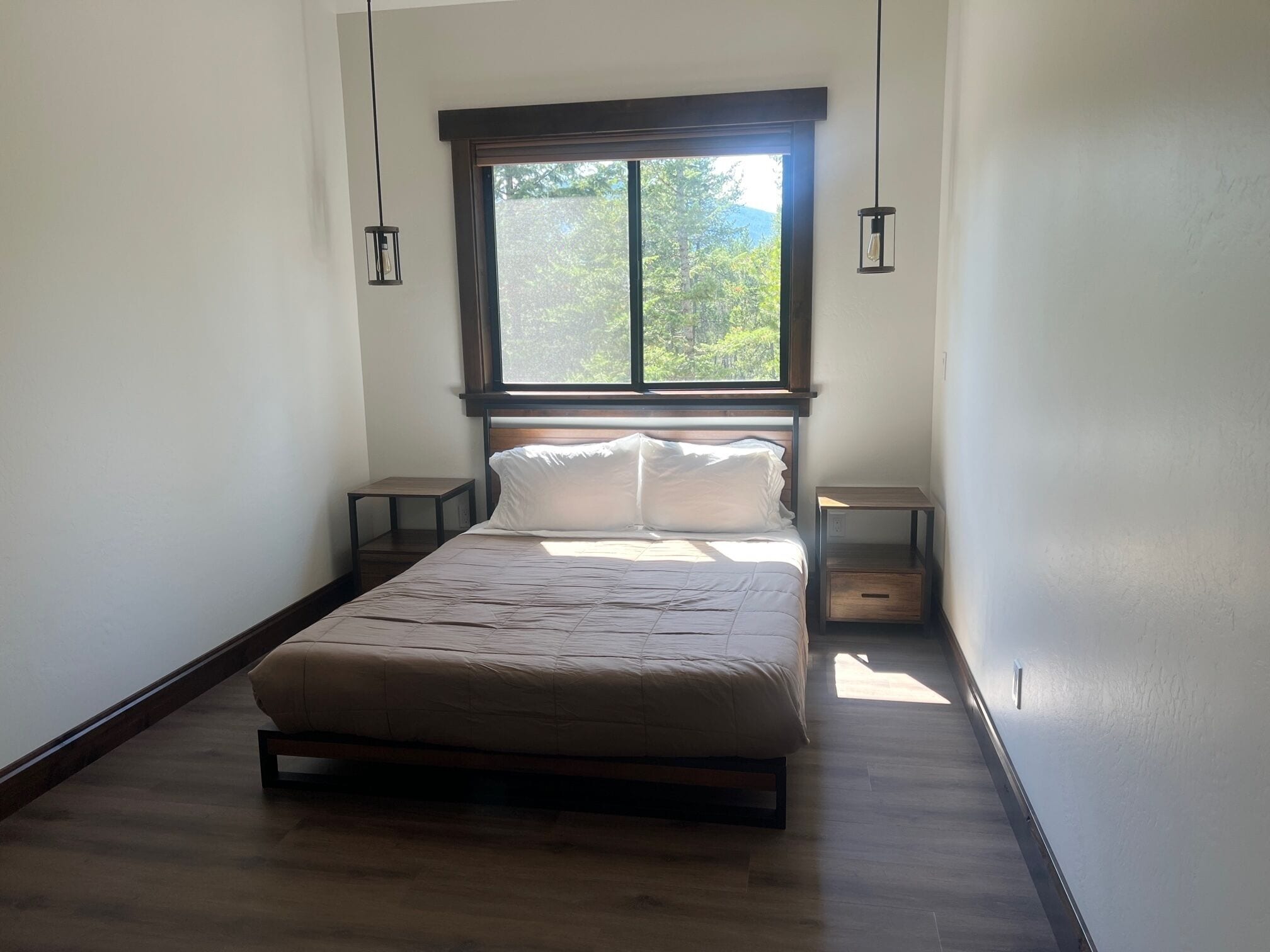 Une chambre avec une grande fenêtre, un lit, deux tables de chevet et des luminaires suspendus.