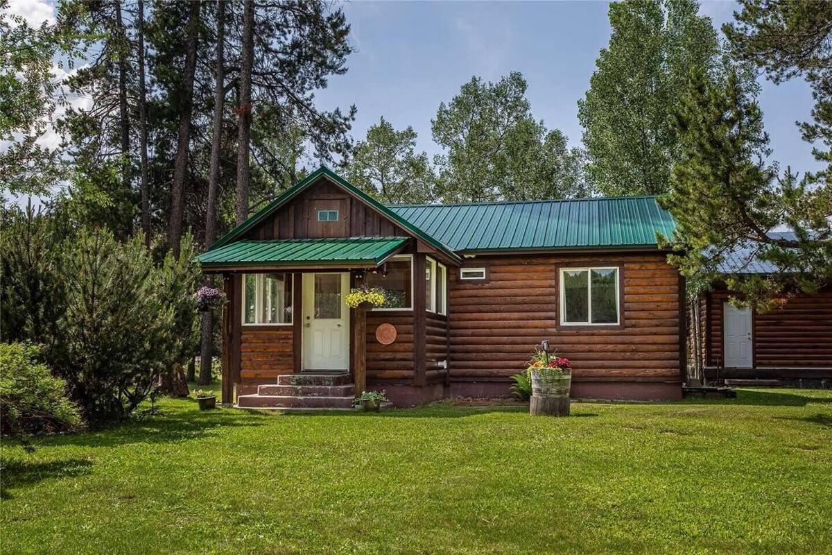 A rustic log cabin with a green metal roof, a front porch, and a well-maintained lawn.