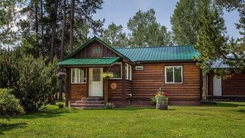 A rustic log cabin with a green metal roof, a front porch, and a well-maintained lawn.