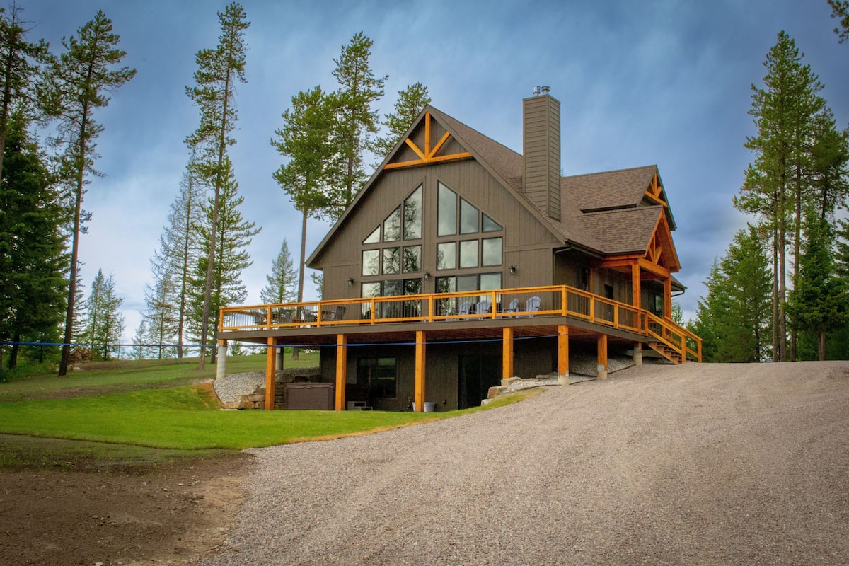 A large, two-story lodge with a prominent balcony and a chimney, surrounded by tall trees.