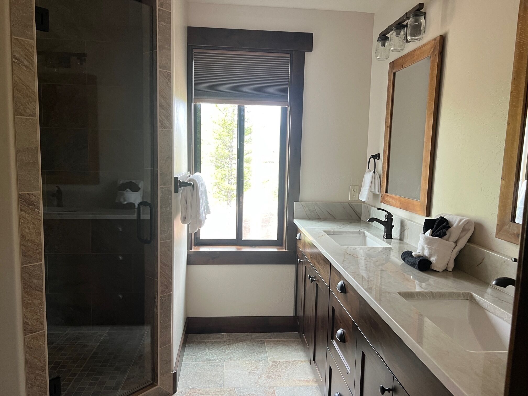 Un baño con cabina de ducha de vidrio, ventana con vistas, lavamanos con espejo y perchero para toallas.