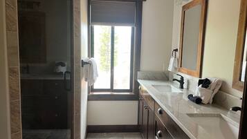 Un baño con cabina de ducha de vidrio, ventana con vistas, lavamanos con espejo y perchero para toallas.