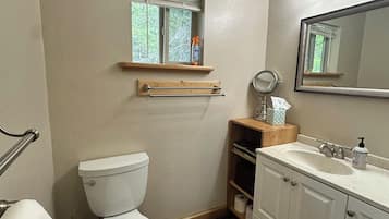 A bathroom with a toilet, sink, mirror, window, and wooden shelves.