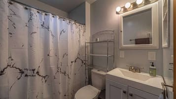 A bathroom with a white toilet, a sink with a mirror above it, and a shower curtain with a marble pattern.