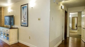 A hallway with wooden flooring, a white wall with a framed abstract painting, a television on a cabinet, and a door leading to another room. - Sandstone Creek Club in Vail for Christmas (Vail)