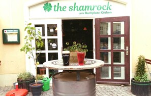 En pub som heter ”The Shamrock”, med en ölkran, ett Guinness-glas och en röd drink på bordet utanför.