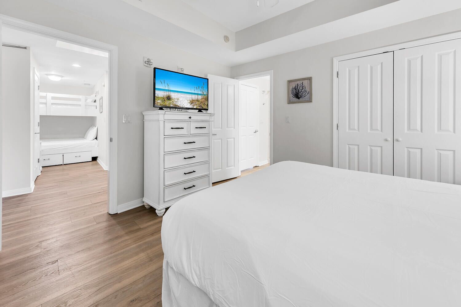 Een slaapkamer met een bed, een dressoir, een televisie, een deur en een muur met een schilderij.
