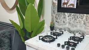 Et køkken med et hvidt komfur, en stor grøn plante, en grå sofa og et rundt spejl på væggen.