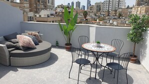En tagterrasse med et rundt bord og stole, en sofa med puder og krukker med planter.