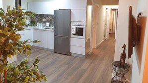 Et moderne køkken med hvide skabe, et rustfrit stål køleskab og en ovn. En plante er i forgrunden, og et lille bord med en giraf-figur står til højre.