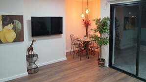 En moderne stue med et fladskærms-TV, et spiseområde med et bord og stole, en dekorativ girafskulptur og en potteplante.