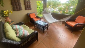 A cozy living area with wicker furniture, a hammock, and a view of lush greenery.