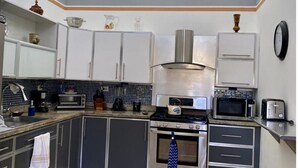 A modern kitchen with white cabinets, a stainless steel range hood, a microwave, a toaster, and a ceiling fan.