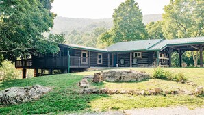 A rustic log cabin with a porch and two chairs, surrounded by a grassy area and large rocks. - Mountaintop cabin in Pearisburg! (Pearisburg)