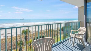 Un balcon avec vue sur la plage et l’océan, une chaise et une petite table.