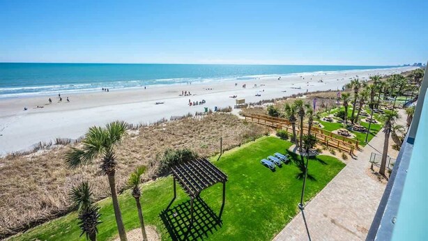 Une vue sur la plage, avec une zone herbeuse, des palmiers et un kiosque.