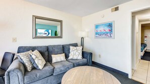 Un salon avec un canapé gris, une table basse ronde, une lampe et un tableau accroché au mur.
