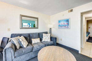 Un salon avec un canapé gris, une table basse ronde, une lampe et un tableau accroché au mur.