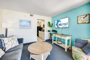 A living room with a sofa, a round table, a TV, and a desk with a plant.