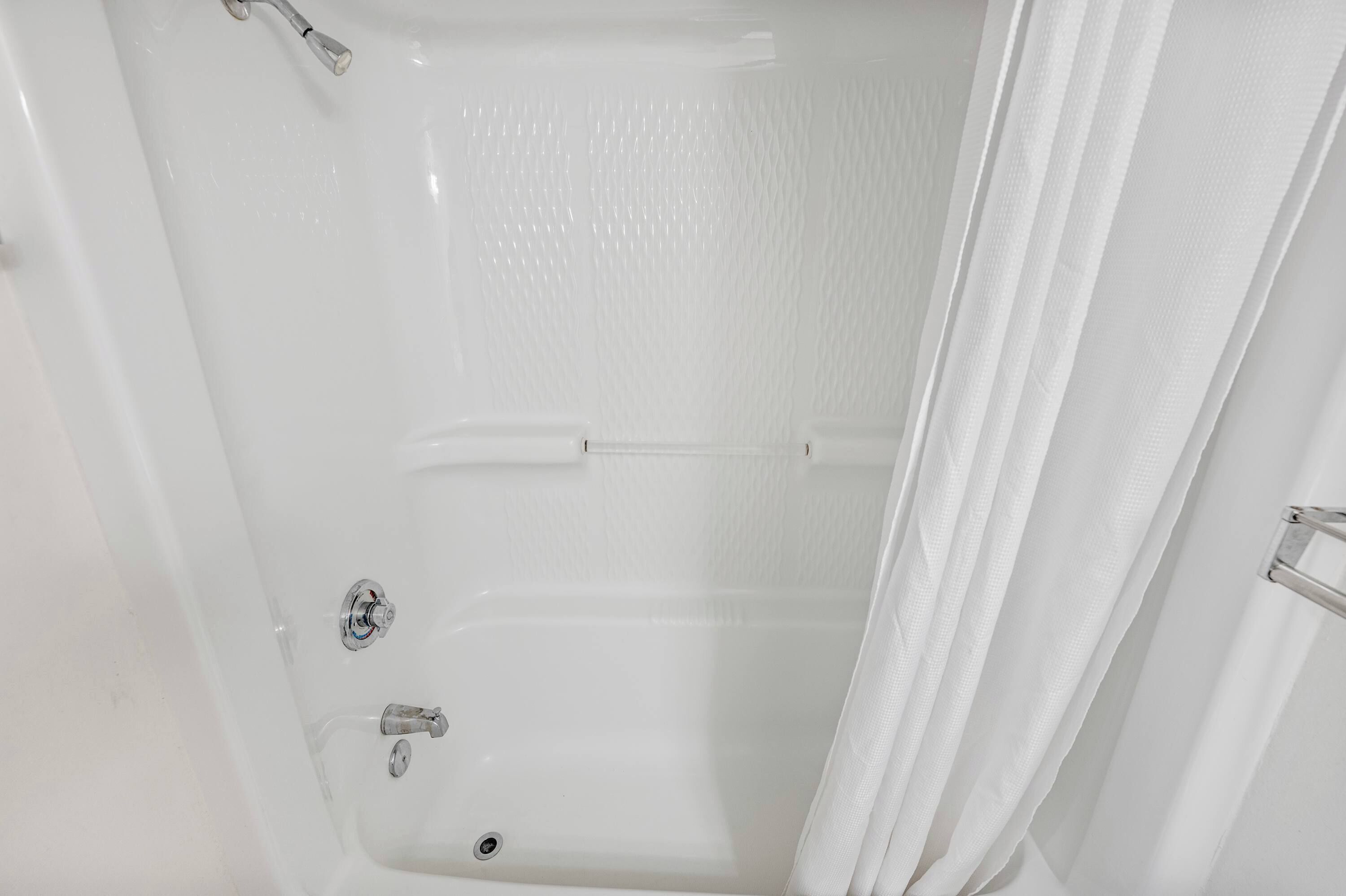 A white bathtub with a shower curtain, a handheld showerhead, and a faucet.