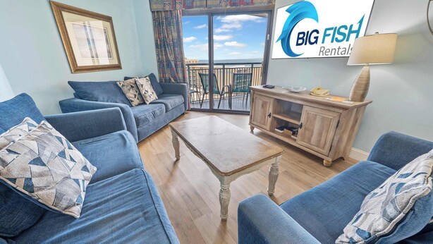 A living room with a sofa set, a coffee table, and a cabinet. There is a view of the outside through a glass door.