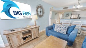 A modern living room with a blue sofa, wooden coffee table, and a TV displaying 'BIG FISH Rentals'.