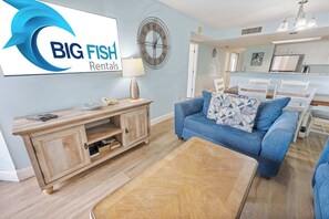 A modern living room with a blue sofa, wooden coffee table, and a TV displaying 'BIG FISH Rentals'.