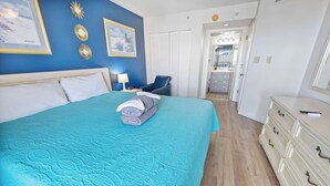 A bedroom with a bed, a chair, a dresser, and a door leading to a bathroom.