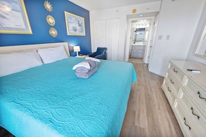 A bedroom with a bed, a chair, a dresser, and a door leading to a bathroom.