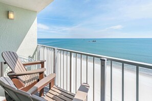 Un balcone con due poltrone Adirondack e un tavolino, con vista su una spiaggia e acque cristalline, con una barca in lontananza.