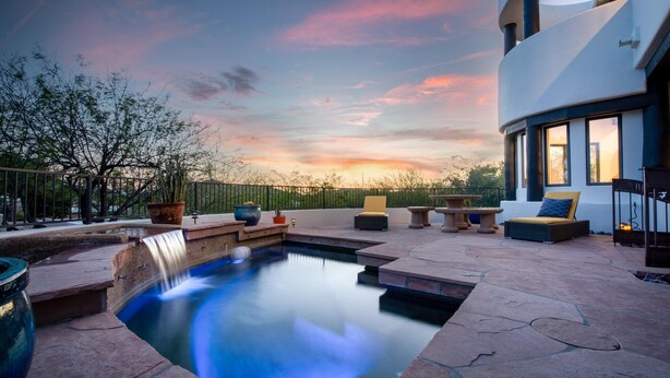 Ein Pool mit Wasserfall, Sitzgelegenheiten im Freien und Blick auf den Sonnenuntergang.