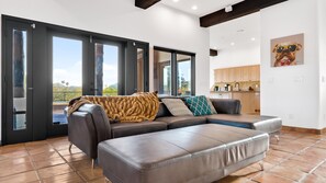 Relax in this stylish living room with a sofa and kitchen area, connected to an outdoor space through a sliding glass door.