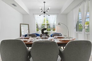 A dining area with a round table, grey chairs, a modern chandelier, and a large letter 'C' centerpiece.