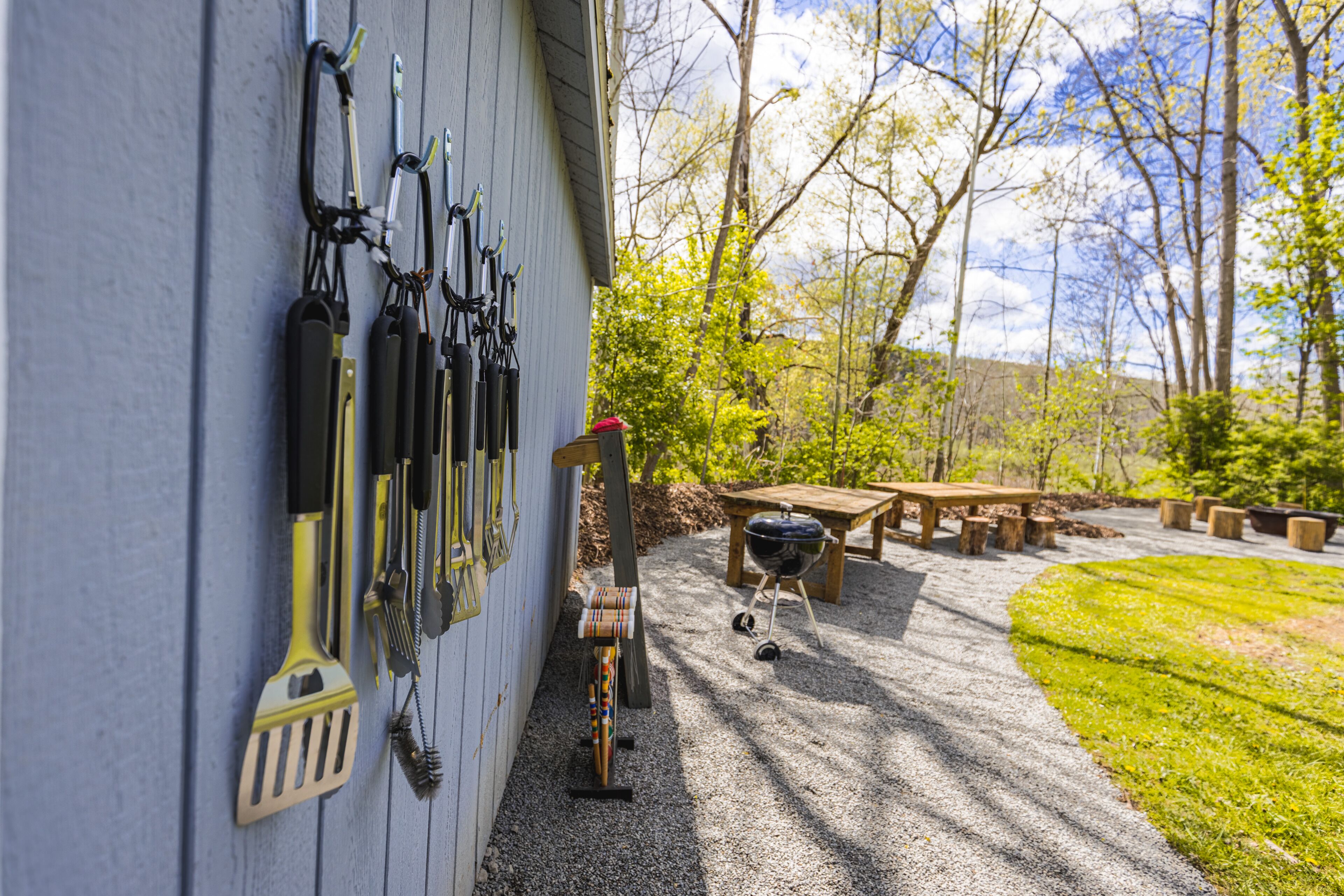 A patio area with a barbecue grill, wooden table, and a wall-mounted tool rack.