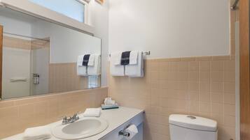 A bathroom with a sink, mirror, towel rack, toilet, and a window with light fixtures.