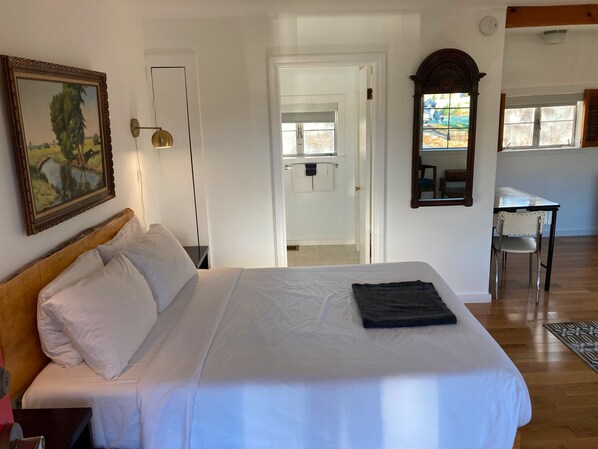 A bedroom with a bed, a painting, a desk, and a chair.