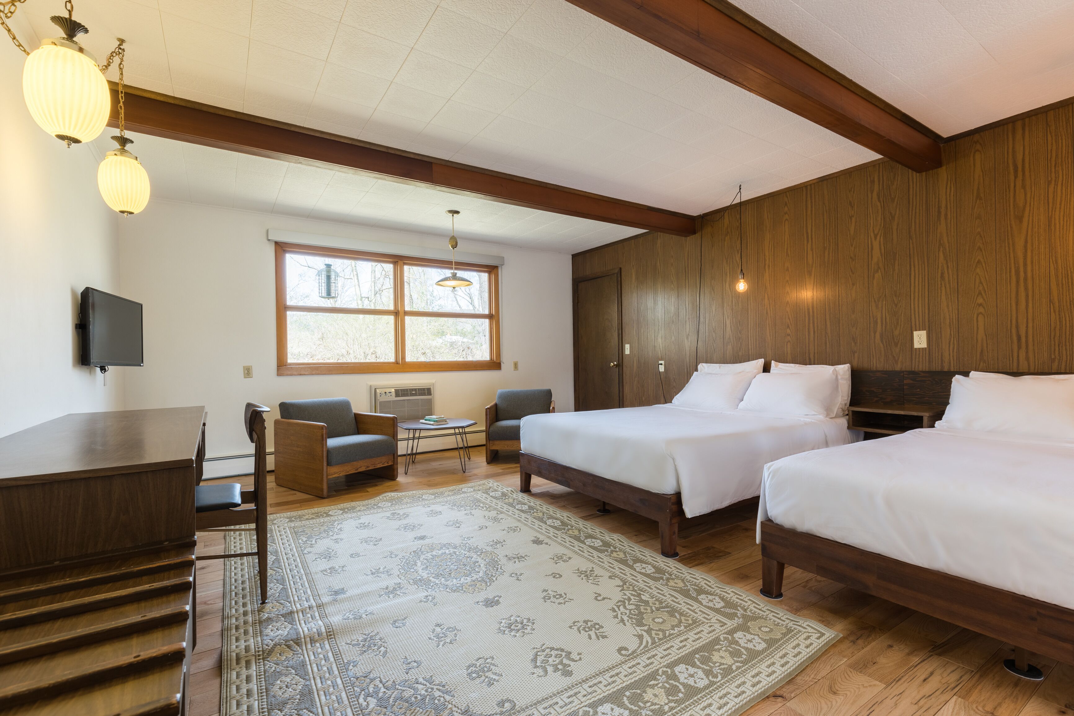 Camera d'albergo con due letti, una scrivania, una sedia, un tavolino e una finestra.