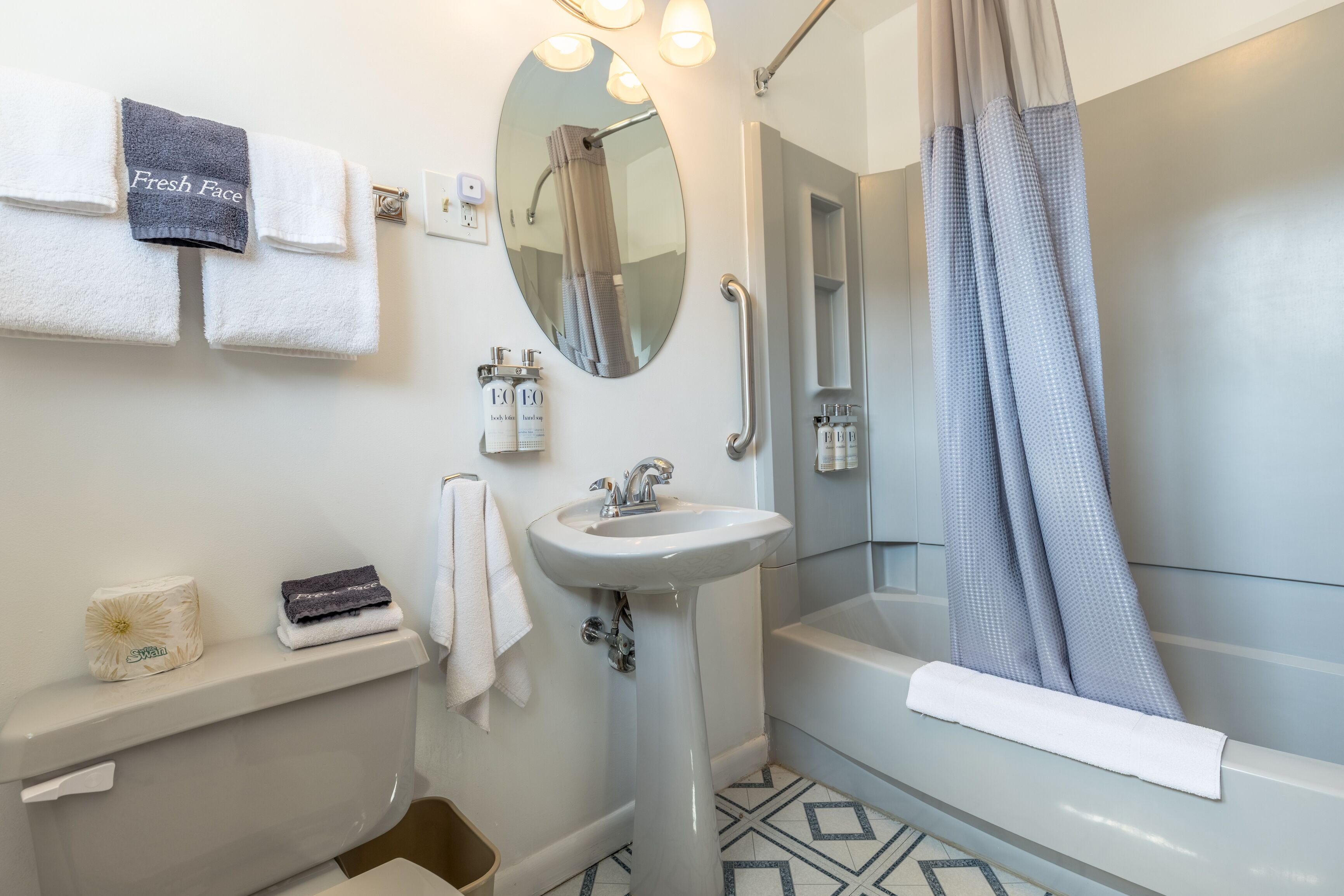 A bathroom with a toilet, sink, and bathtub. There are towels and toiletries on the sink area.