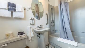 A bathroom with a toilet, sink, and bathtub. There are towels and toiletries on the sink area.