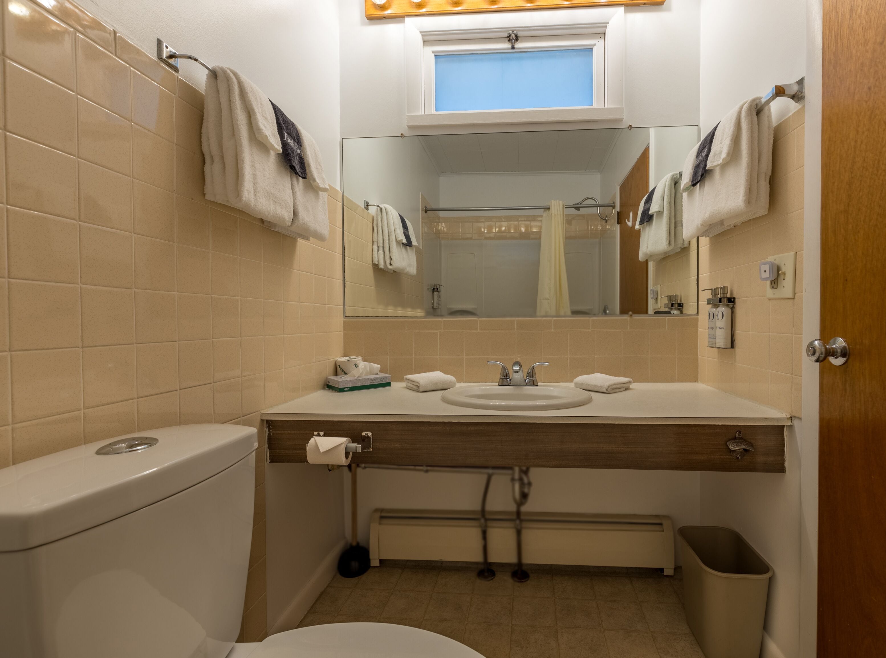 A bathroom with a toilet, sink, mirror, and a window above the mirror.