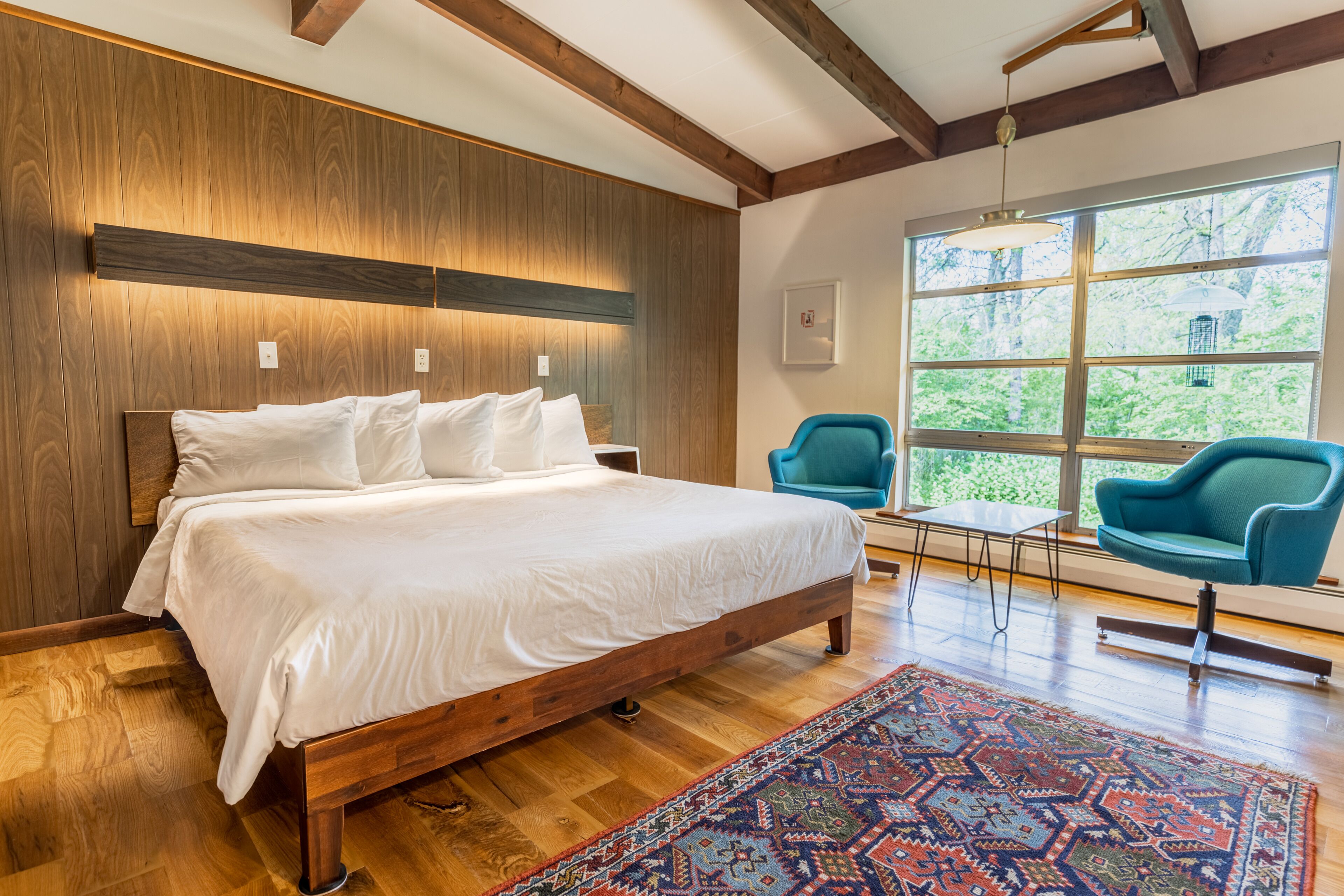 A bedroom with a wooden bed, a blue chair, and a large window with a view of trees.