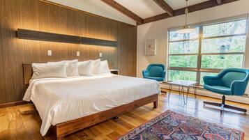 A bedroom with a wooden bed, a blue chair, and a large window with a view of trees.