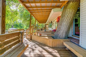 Une terrasse en bois dotée d’un espace abrité, un grand tronc d’arbre et une maison avec un porche.