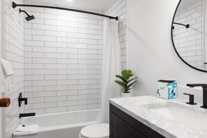 A modern bathroom with white subway tiles, a white bathtub, a toilet, a black faucet, a white sink, and a mirror. - Outpost: Woodlands A5 (Wilson)