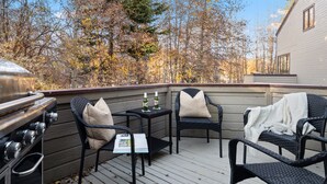 Eine Terrasse mit Gartenmöbeln, einem Grill und Blick auf Bäume und ein Haus.